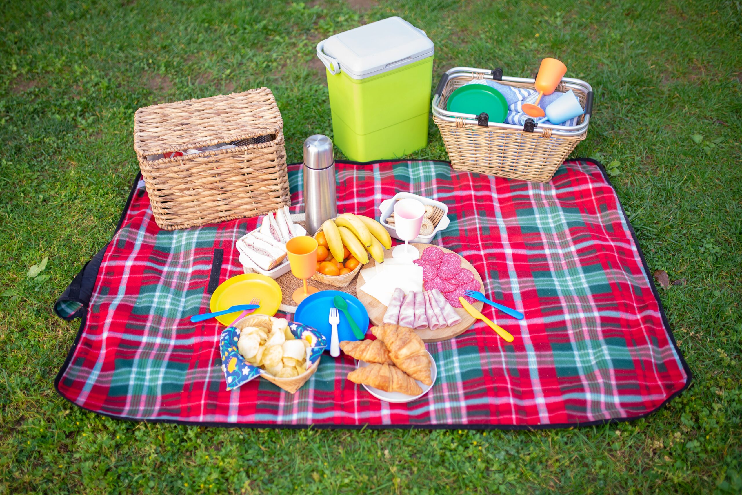 Picnic food arranged on a blanket with a cooler nearby for keeping perishable foods cold