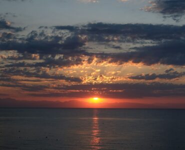 The Sun setting near a flat horizon under scattered clouds