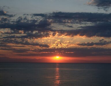 The Sun setting near a flat horizon under scattered clouds