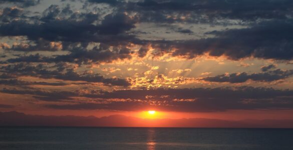 The Sun setting near a flat horizon under scattered clouds