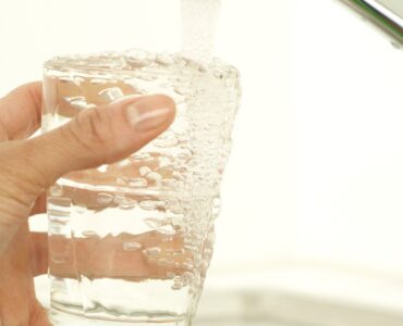Tap water filling a clear drinking glass from a kitchen faucet.