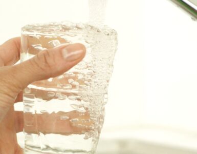 Tap water filling a clear drinking glass from a kitchen faucet.