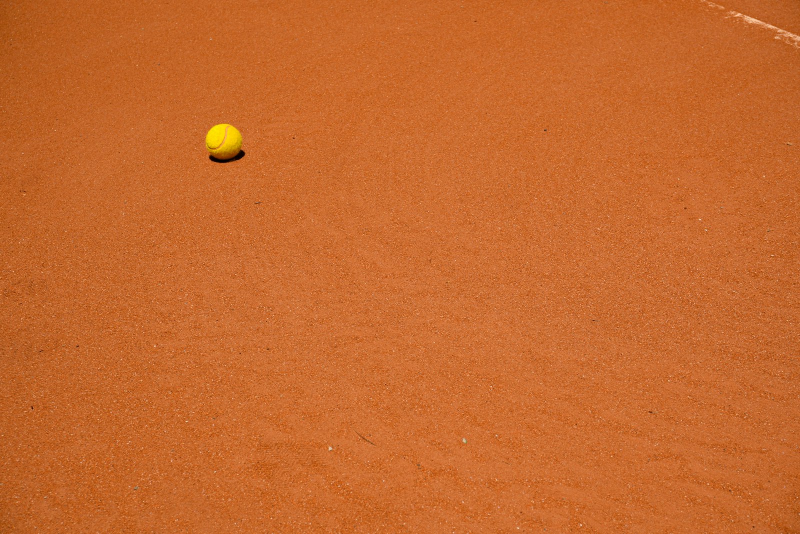A tennis ball sitting on a red clay court surface