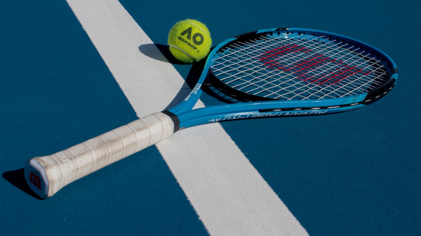 A tennis racket and ball on a blue hard court