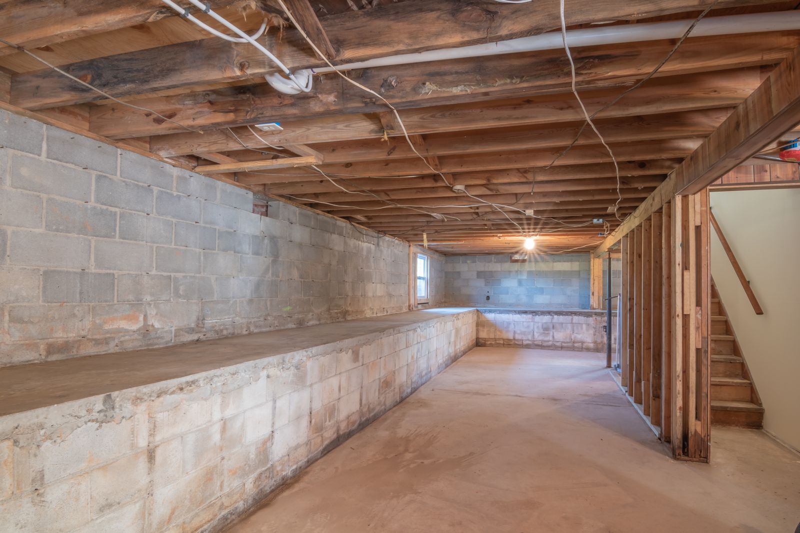 An unfinished basement with concrete walls and exposed beams