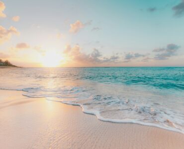 Bright sunlight over a sandy beach and blue ocean water.