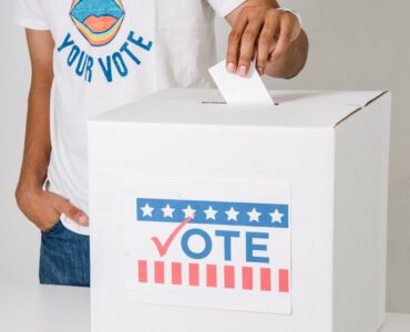 A voter places a ballot into a white box marked Vote