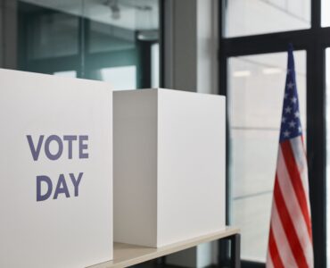 White voting booths labeled Vote Day beside an American flag