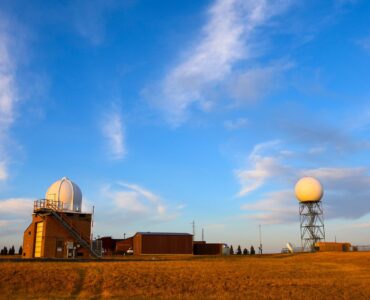 A weather radar station in an open field used to monitor storms and improve forecasts.