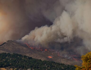 A large wildfire smoke plume rising above hills and fields