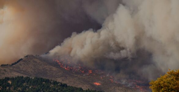 A large wildfire smoke plume rising above hills and fields