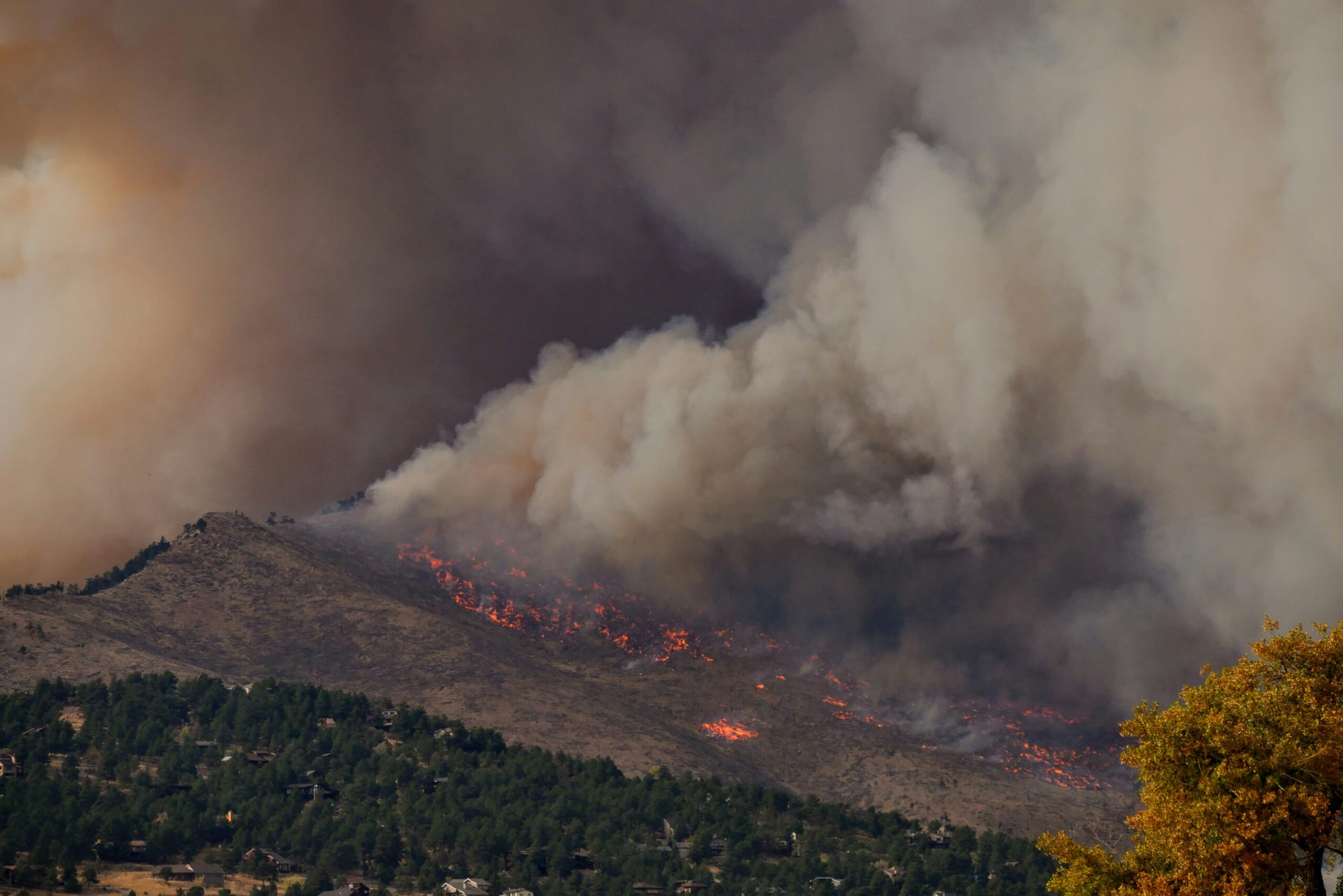A large wildfire smoke plume rising above hills and fields