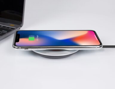 A smartphone resting on a wireless charging pad beside a laptop