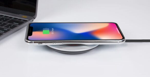 A smartphone resting on a wireless charging pad beside a laptop