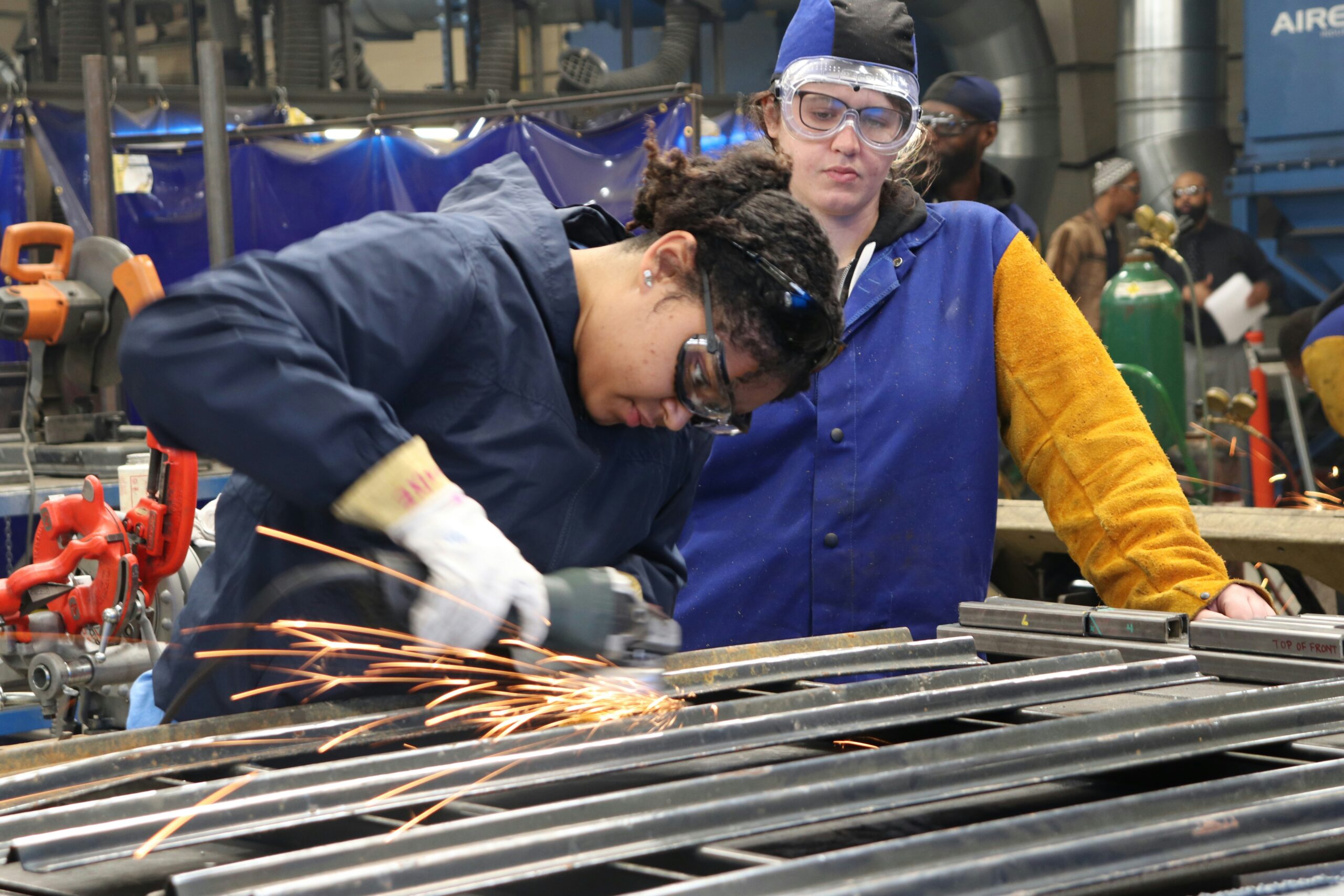Students wearing protective eyewear practice metalwork in a career training workshop