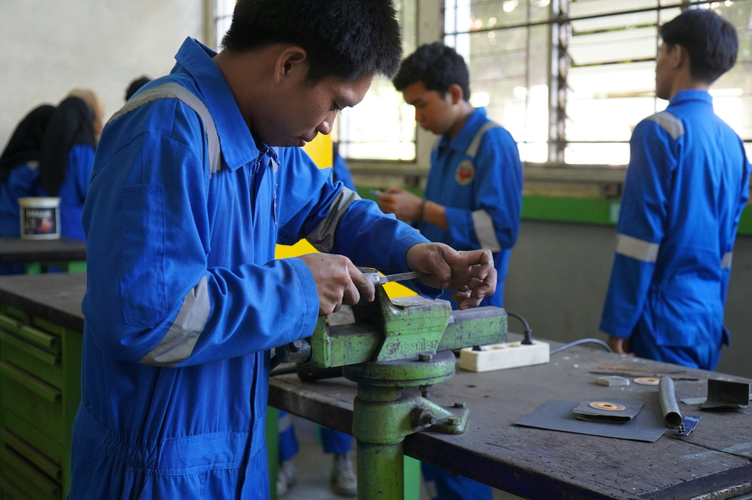 A student in a blue uniform works with hand tools in a technical training workshop