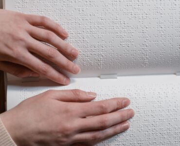 Hands reading raised Braille dots across an open book.
