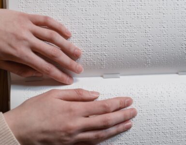 Hands reading raised Braille dots across an open book.