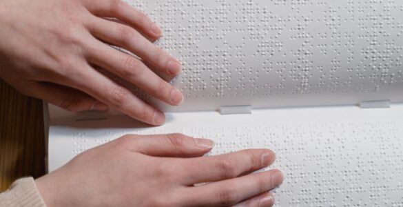 Hands reading raised Braille dots across an open book.