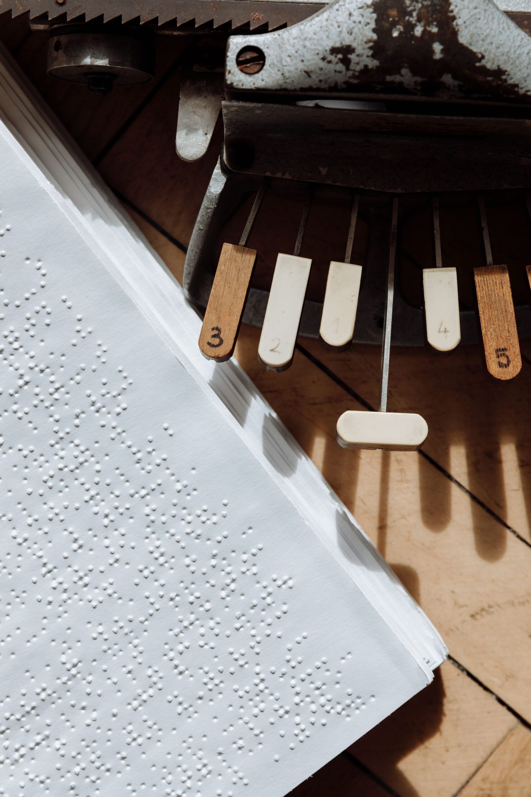 A Braille typewriter beside a page covered with raised Braille dots.