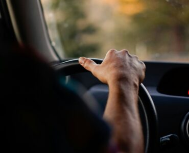 A driver holds the steering wheel while scenery blurs outside the car window
