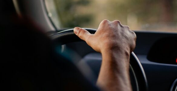 A driver holds the steering wheel while scenery blurs outside the car window