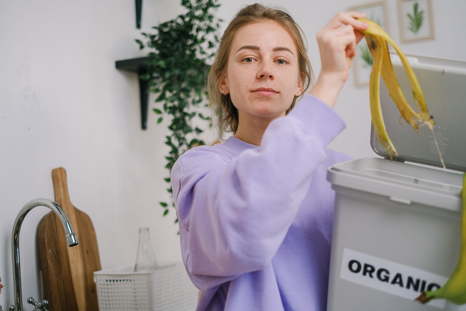 A person places a banana peel into an organic waste bin while preparing food in a kitchen.