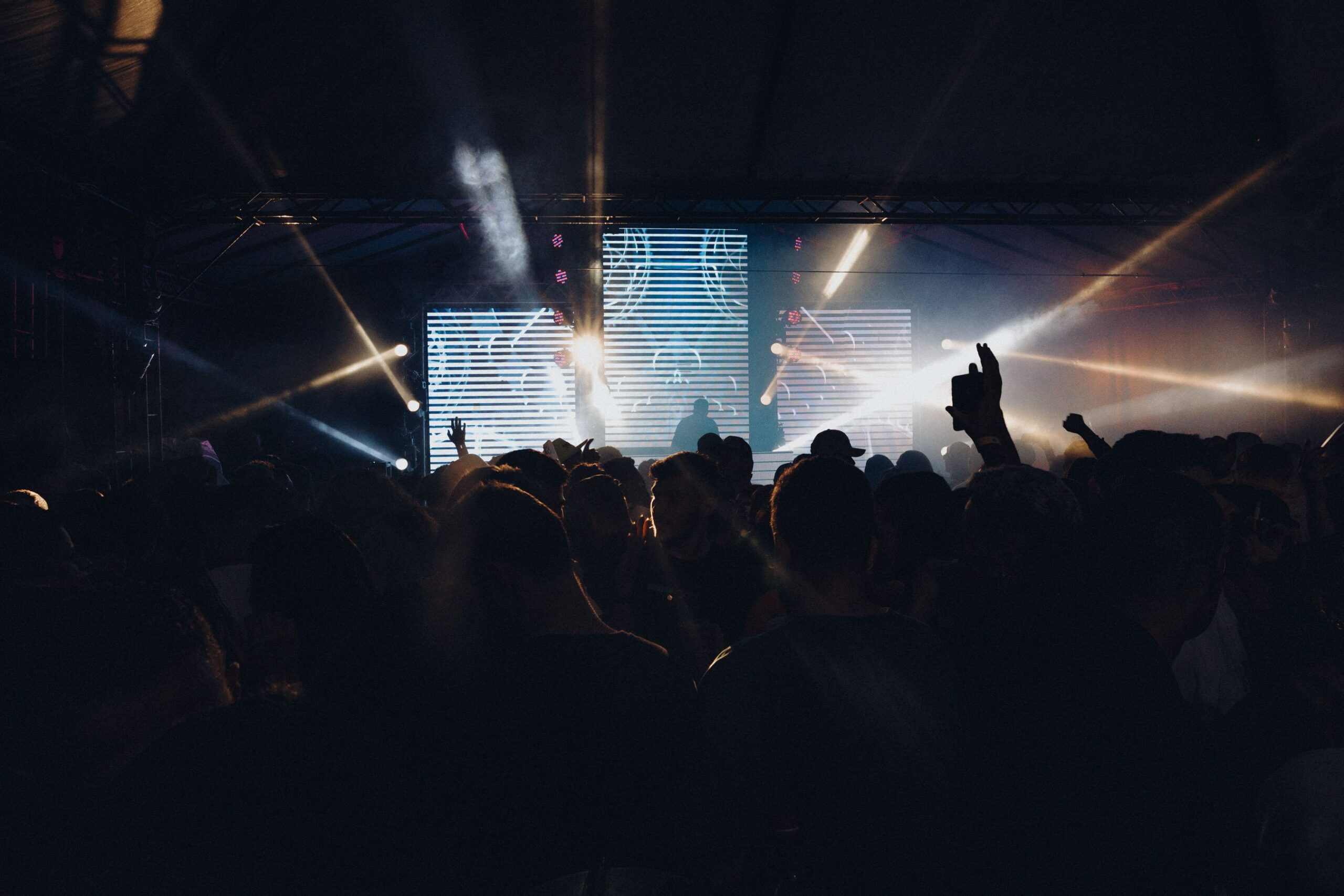 A concert crowd facing a brightly lit stage with sound and lighting equipment