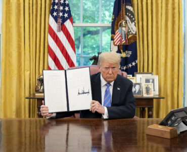 A president signs and displays an executive order at the Resolute Desk in the Oval Office.