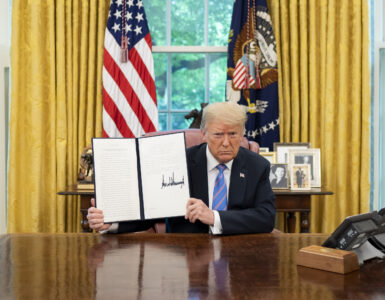 A president signs and displays an executive order at the Resolute Desk in the Oval Office.