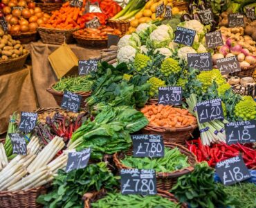 A farmers market vegetable stall with baskets of produce and handwritten price signs