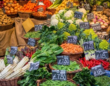 A farmers market vegetable stall with baskets of produce and handwritten price signs