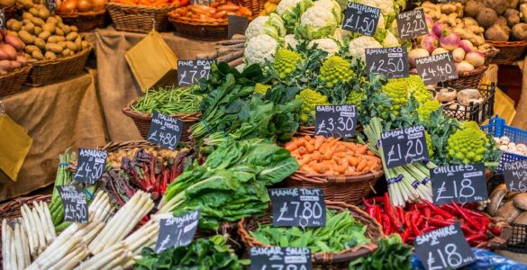 A farmers market vegetable stall with baskets of produce and handwritten price signs