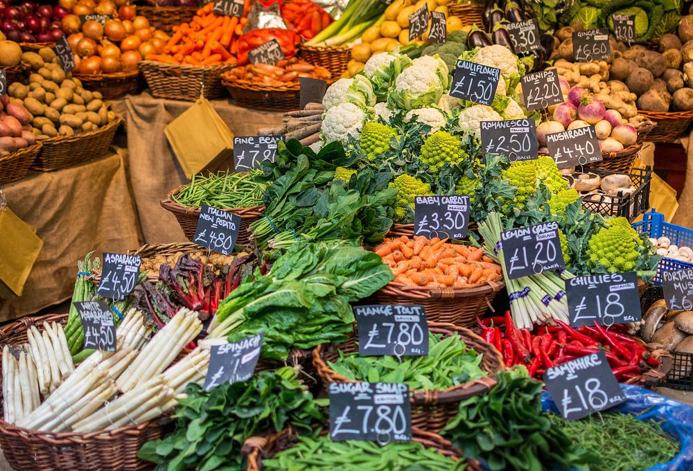 A farmers market vegetable stall with baskets of produce and handwritten price signs