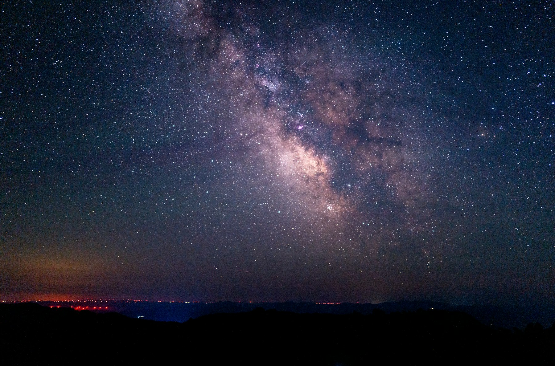 The Milky Way glowing over a dark horizon with faint city lights in the distance
