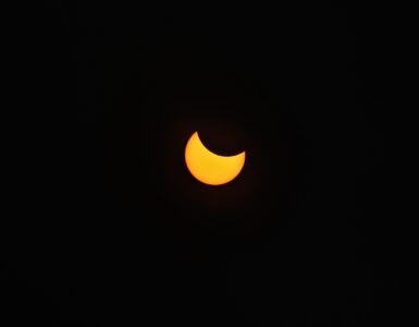 A partial solar eclipse with the Moon covering part of the Sun against a dark sky.