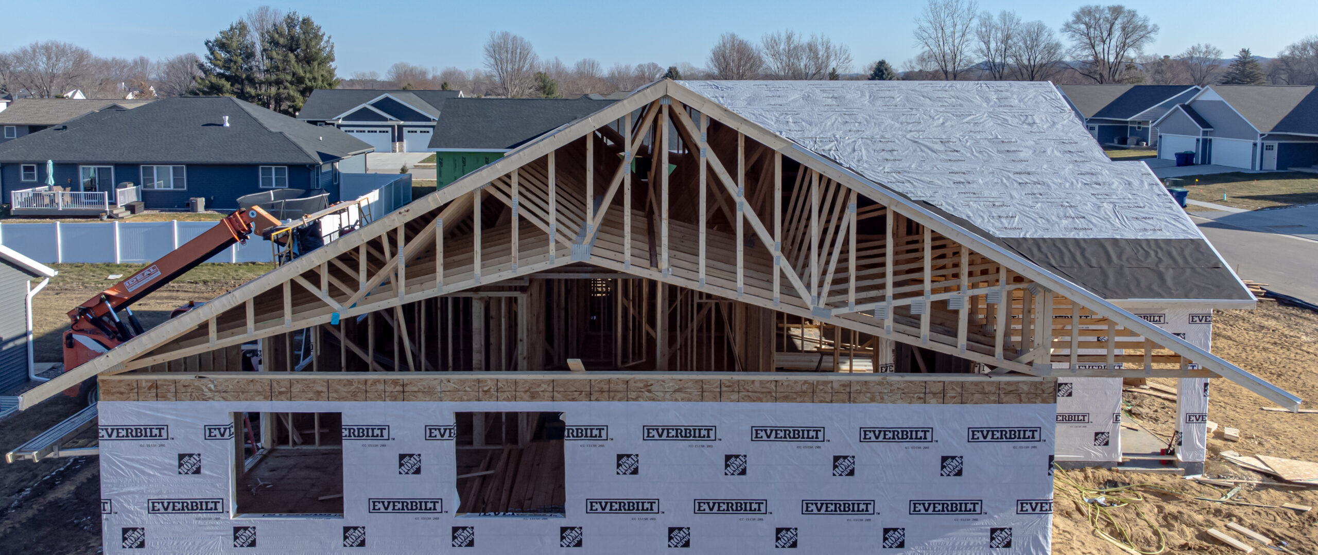 Wooden roof framing with triangular trusses visible inside a house under construction.
