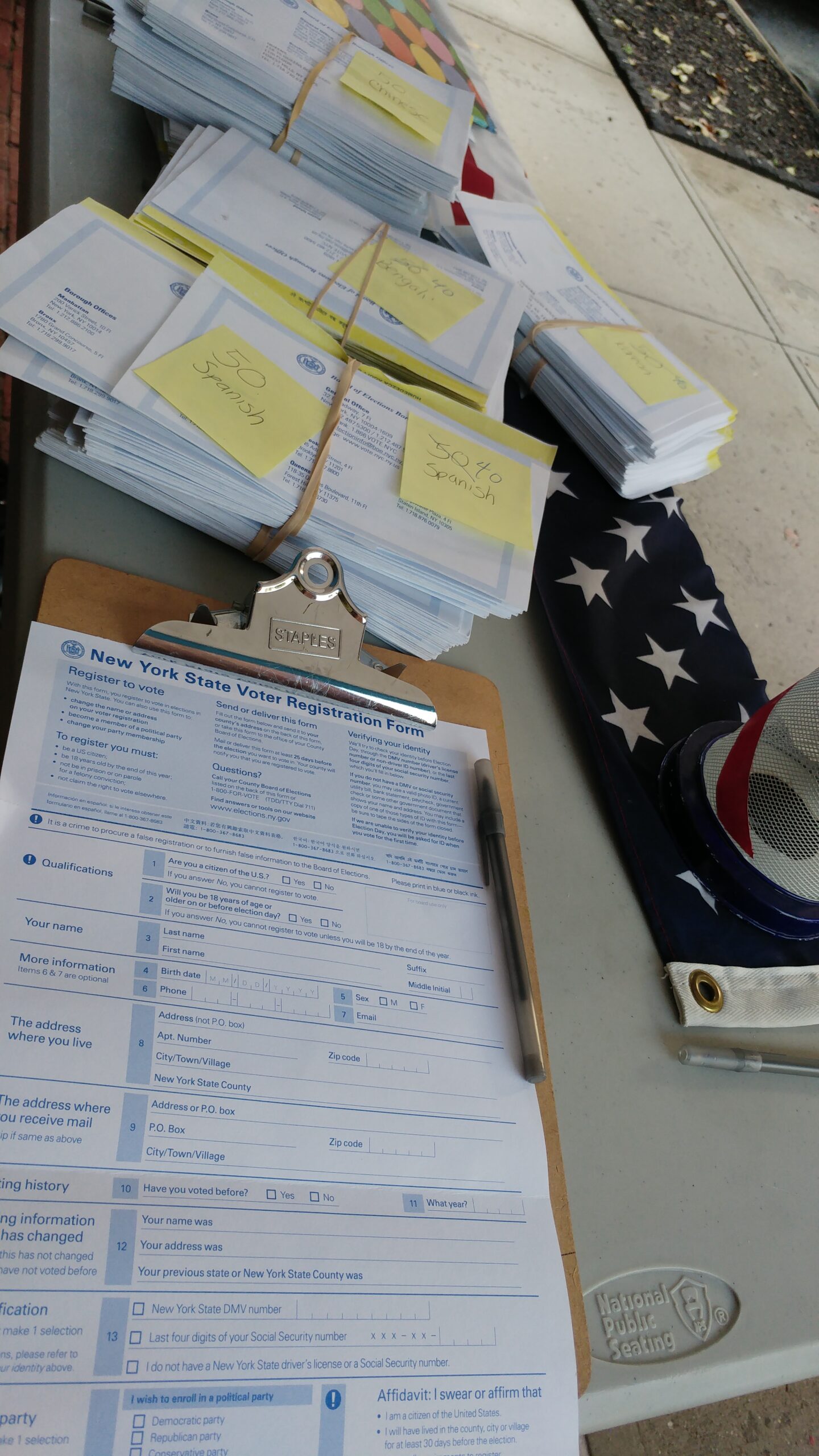 Voter registration forms on a clipboard with a pen and multilingual forms nearby