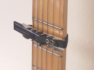 A capo clamped across the strings on a guitar neck