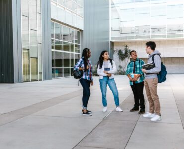 College students walking near a campus building while planning how to request academic accommodations before classes start.