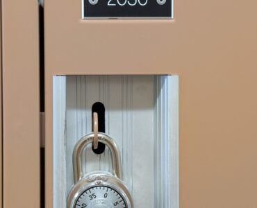 A combination lock hanging on a school locker, showing the rotating dial used to enter a number sequence.