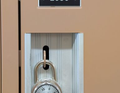A combination lock hanging on a school locker, showing the rotating dial used to enter a number sequence.