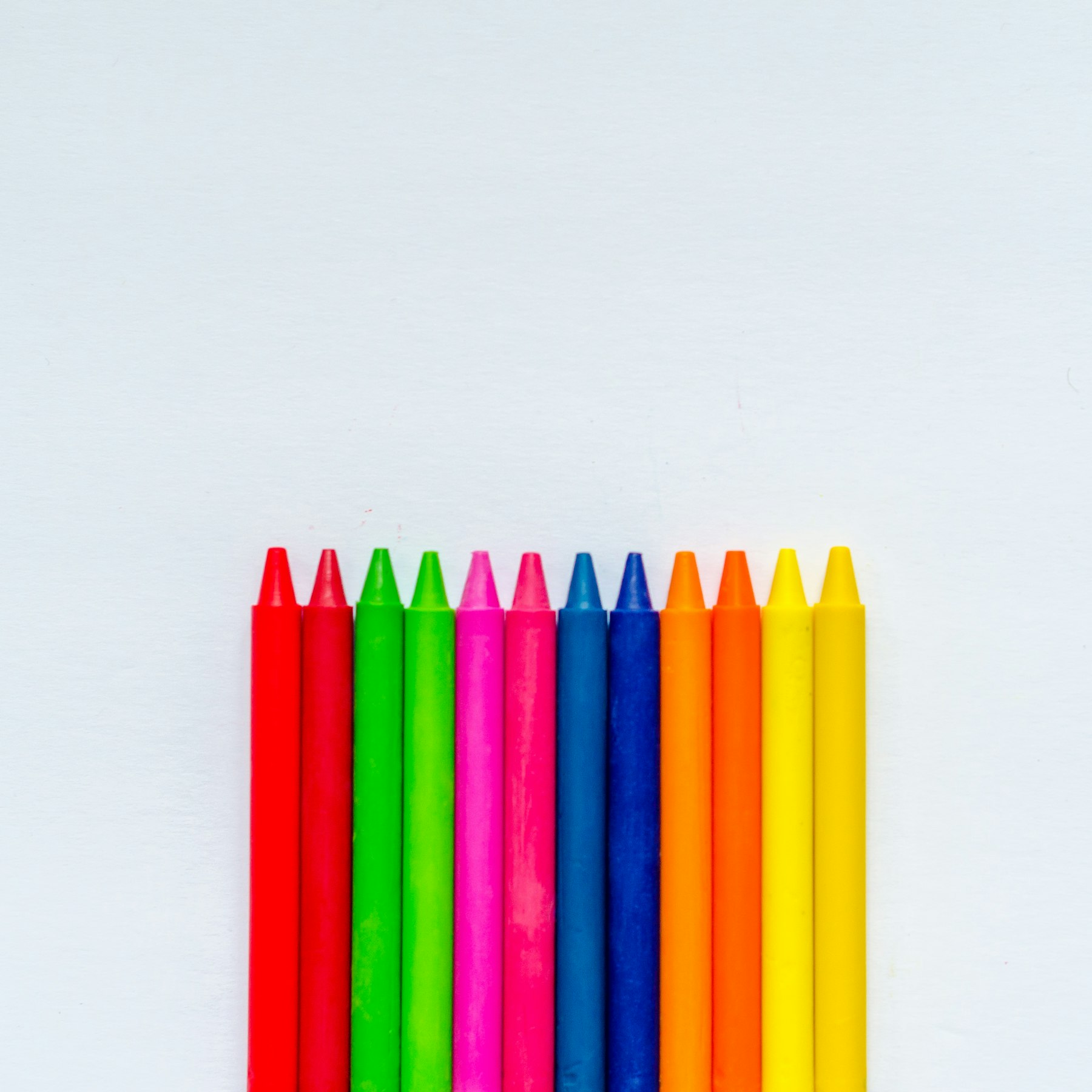 Bright crayons arranged on white paper, showing the range of pigments used in everyday coloring tools.