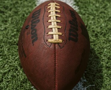 A close view of an American football with its laces aligned on a turf field.