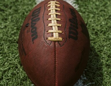 A close view of an American football with its laces aligned on a turf field.