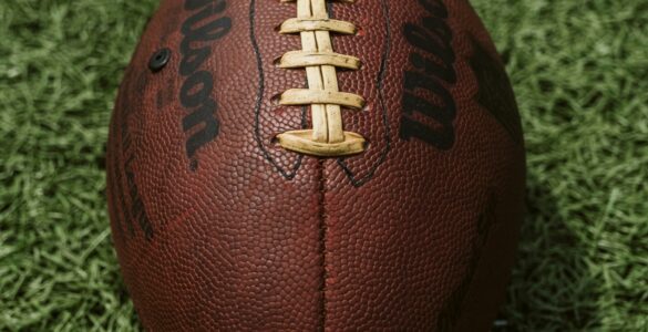 A close view of an American football with its laces aligned on a turf field.