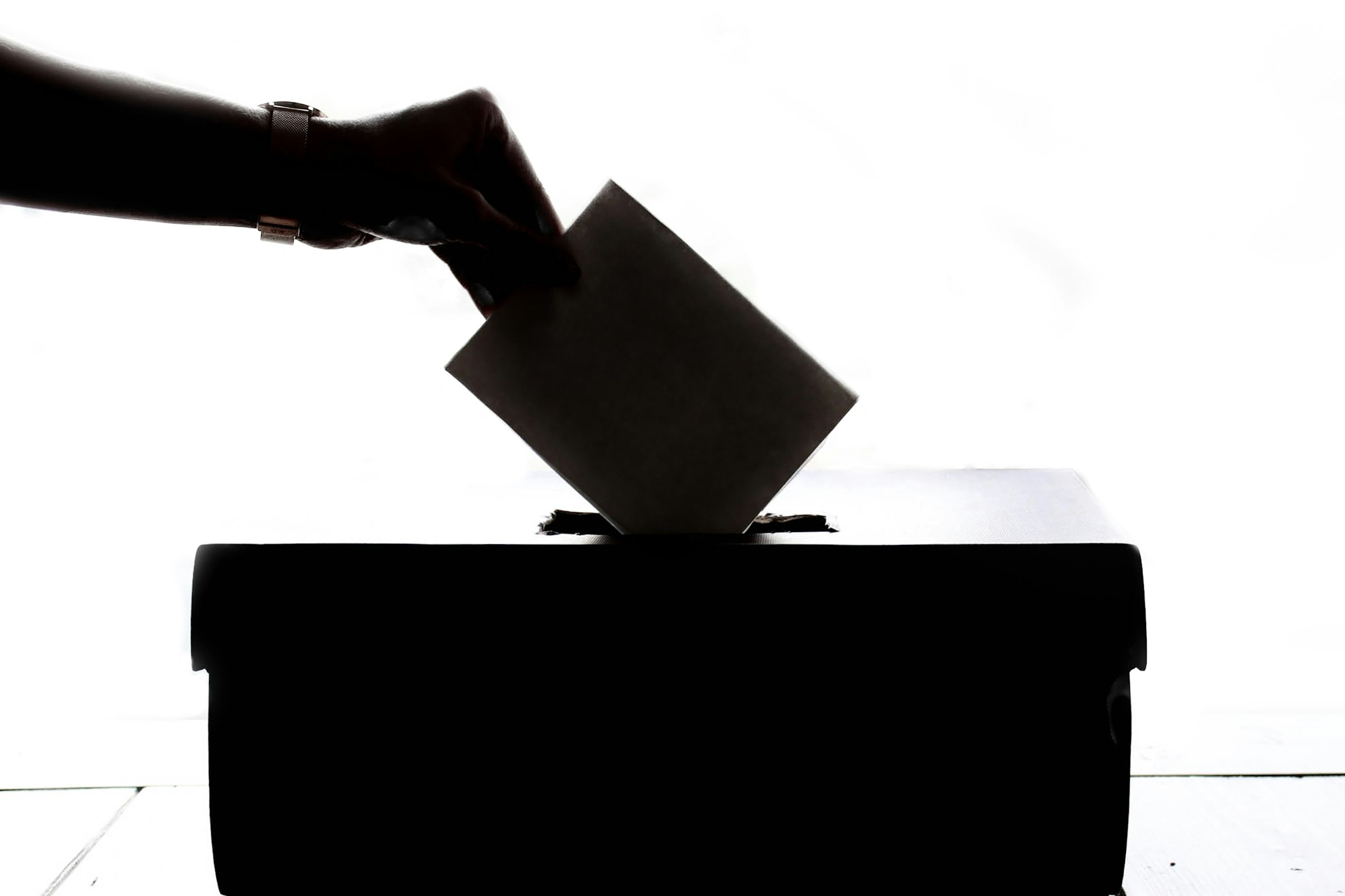A hand places a paper ballot into a ballot box during an election.