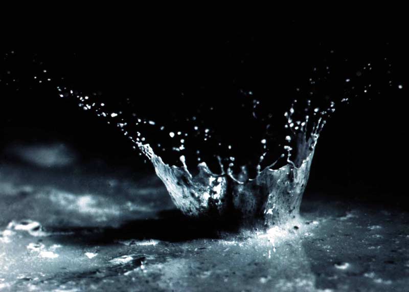 A single raindrop splashes soil and water upward, showing how rain can lift tiny particles into the air.