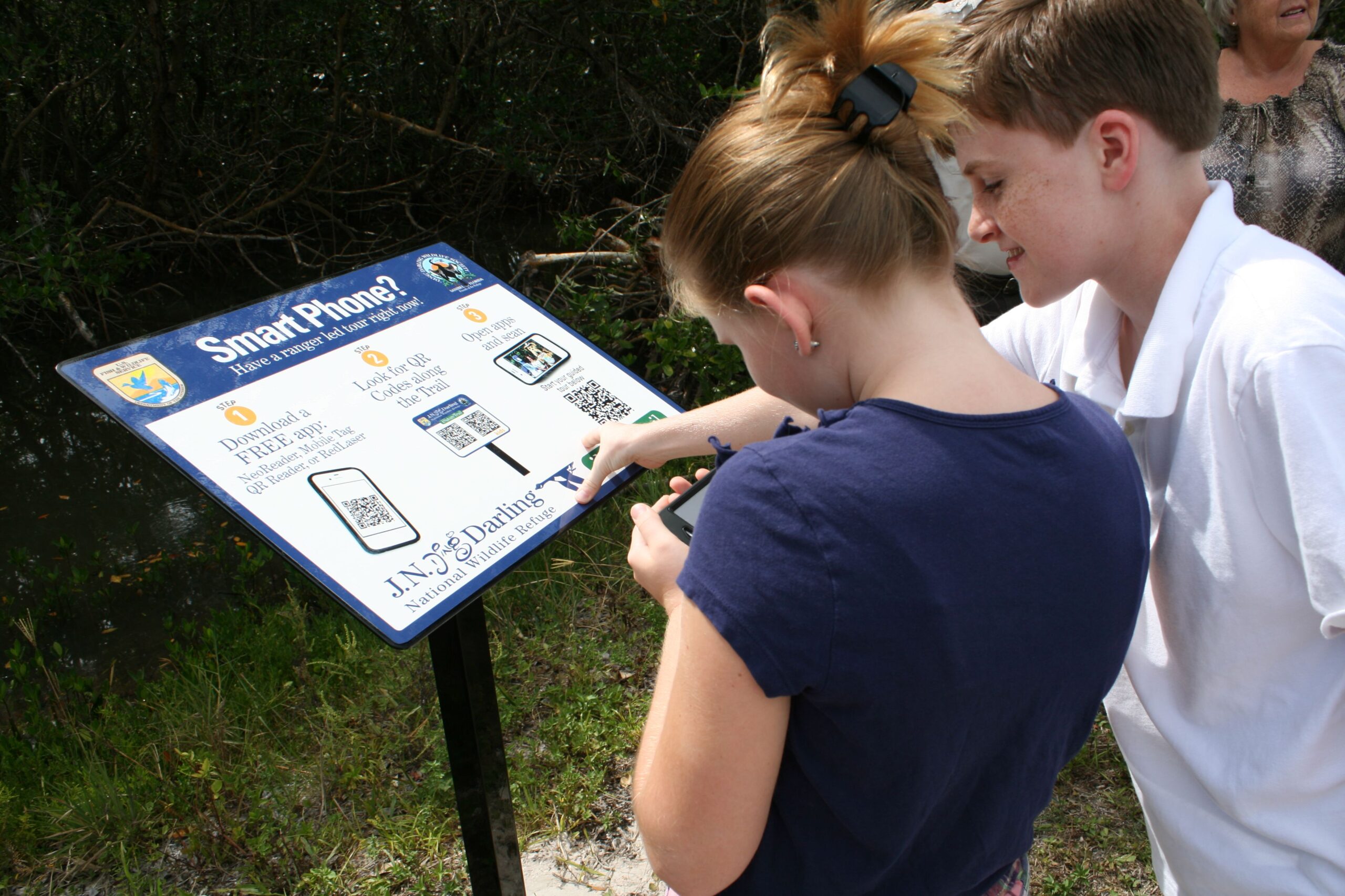 Visitors scan QR codes on a public information sign, showing how small printed codes can connect people to digital information.
