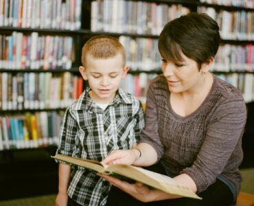 A student and adult read together in a library while discussing a passage for reciprocal teaching.
